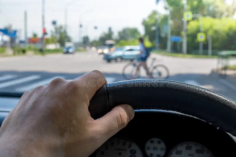 mano-de-hombre-en-el-volante-un-auto-frente-paso-peatonal-la-del-conductor-al-coche-fondo-y-una-ciclista-cruzando-carretera-191420252